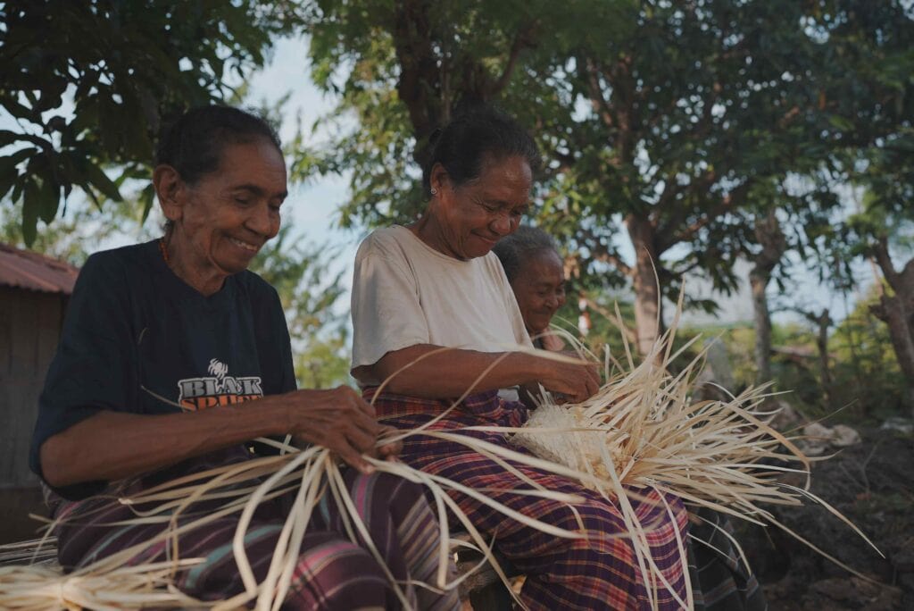 tiga orang wanita sedang menganyam sebuah keranjang anyaman dari daun lontar khas Flores NTT sambil tersenyum
