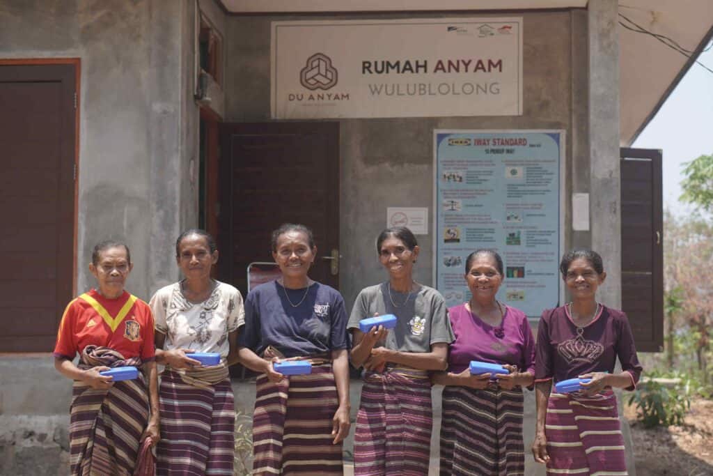 enam orang wanita penganyam yang tersenyum di depan rumah anyam Wulublolong Du Anyam yang berada di NTT